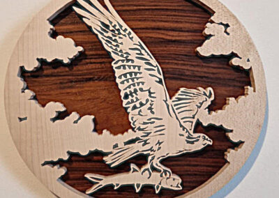 Tableau circulaire en bois chantourné représentant un aigle en plein vol capturant un poisson, marqueterie artisanale en érable sur fond noyer