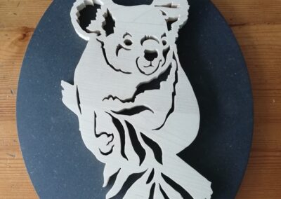 Tableau en bois chantourné koala sur une branche d'eucalyptus, décoration murale ovale artisanale en érable sur fond valchromat noir